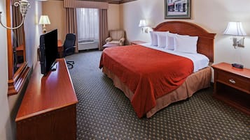 Une chambre d’hôtel avec un grand lit, un bureau avec un ordinateur, une chaise, une lampe et une fenêtre avec des rideaux.