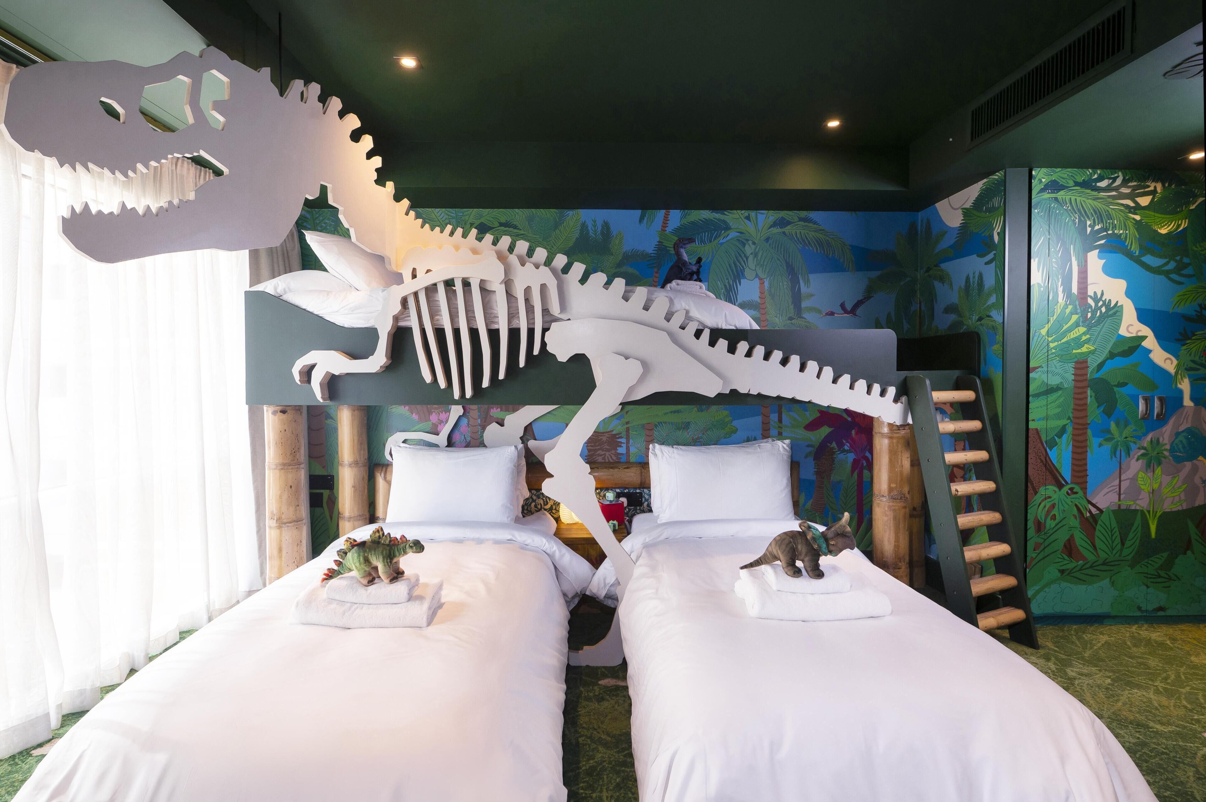 Una habitación con dos camas, una decoración de esqueleto de dinosaurio y un mural de una escena selvática.