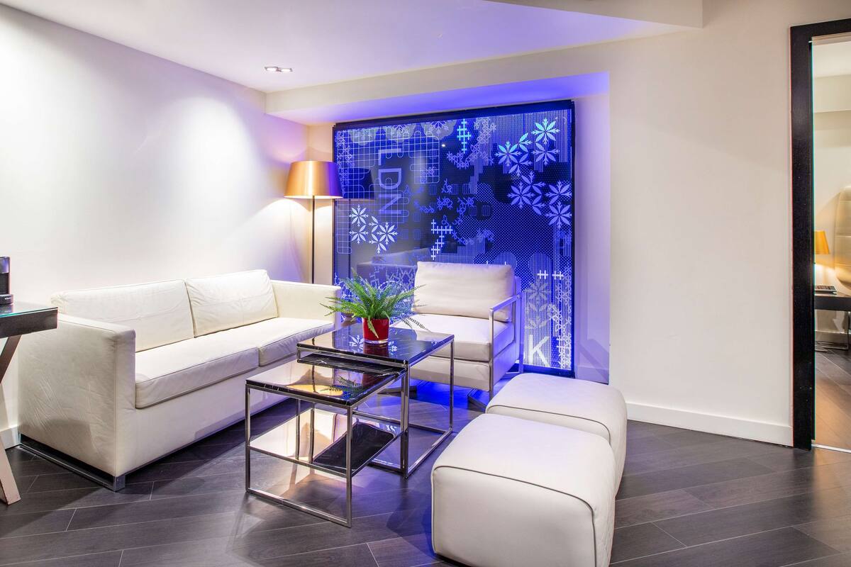 Una sala de estar moderna con un sofá blanco, una mesa de centro de vidrio y un panel decorativo con patrones geométricos.