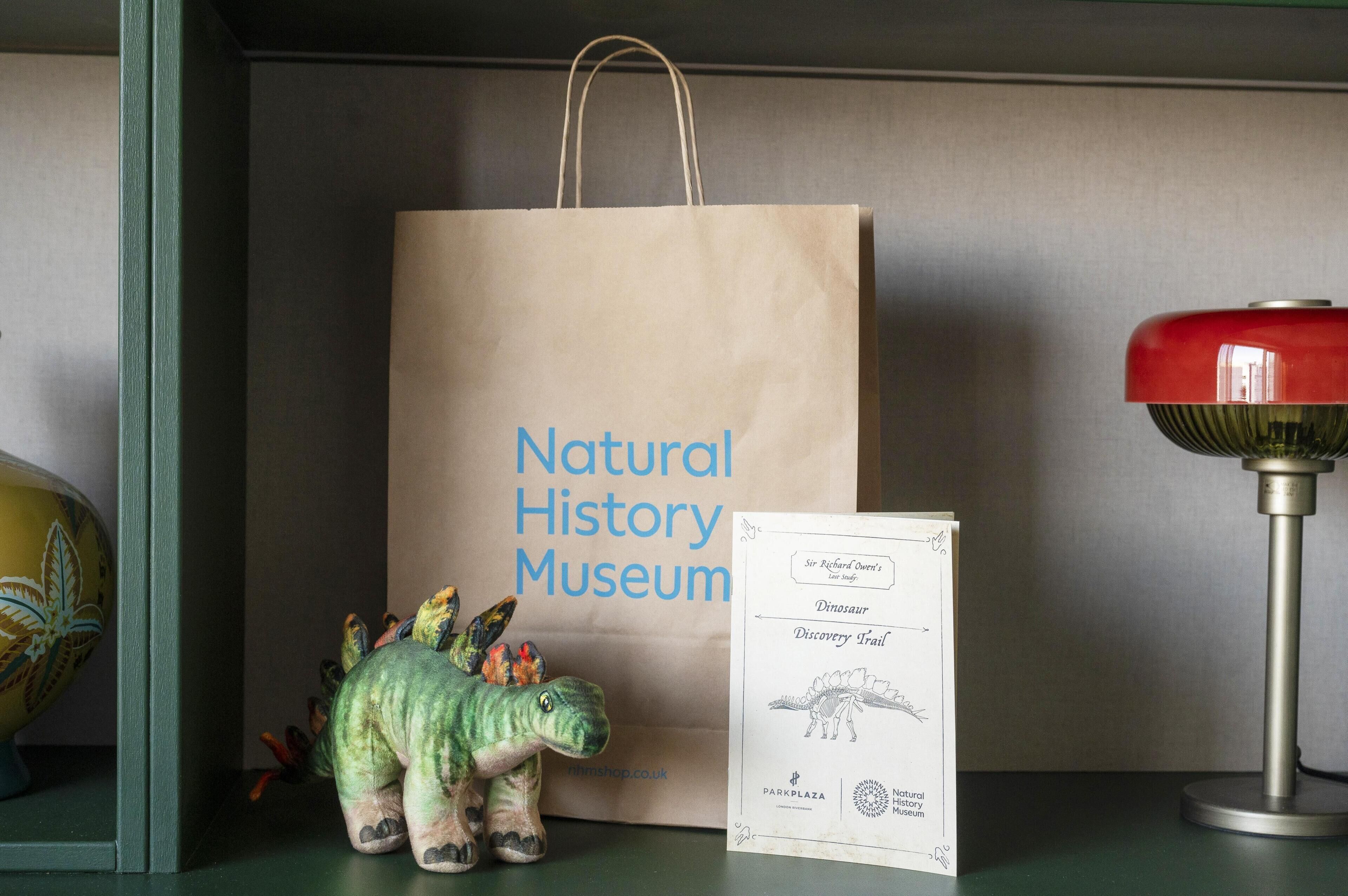 A dinosaur toy, a paper bag with 'Natural History Museum' text, and a lamp.