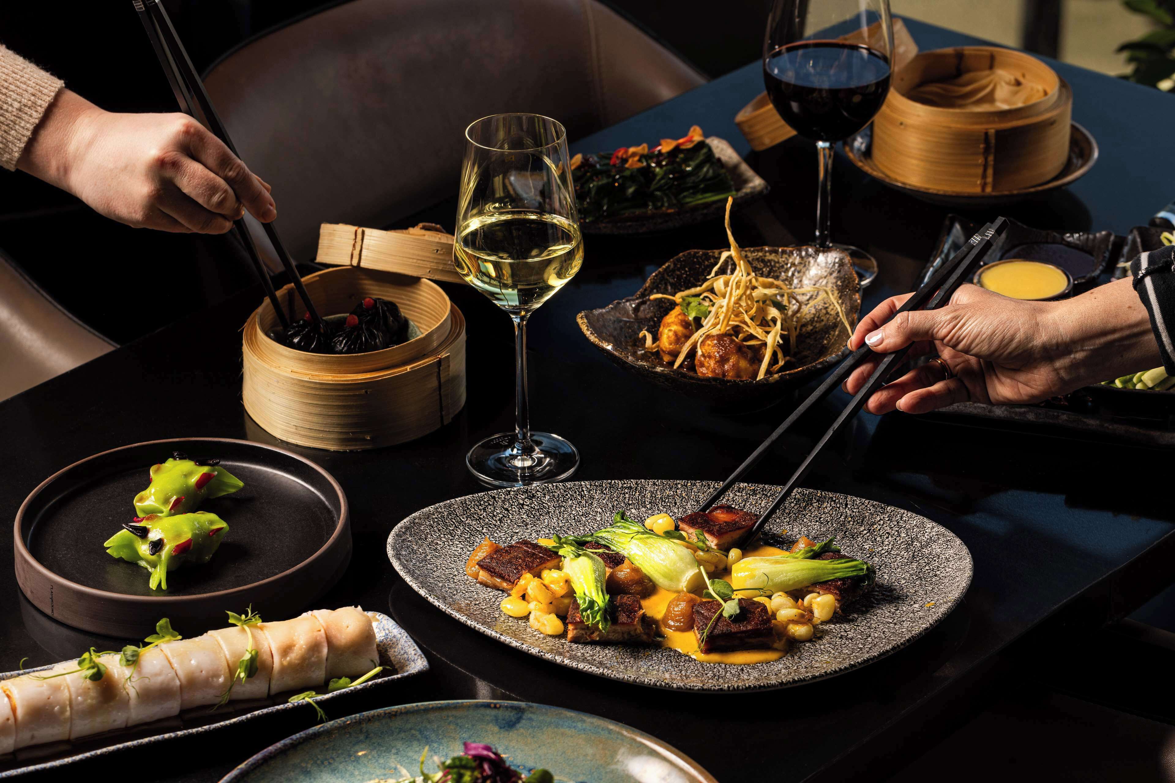 A dining table with various dishes, chopsticks, and wine glasses.