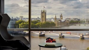 Una habitación con un amplio ventanal que da a un río con puentes y edificios históricos, incluyendo una destacada torre de reloj.