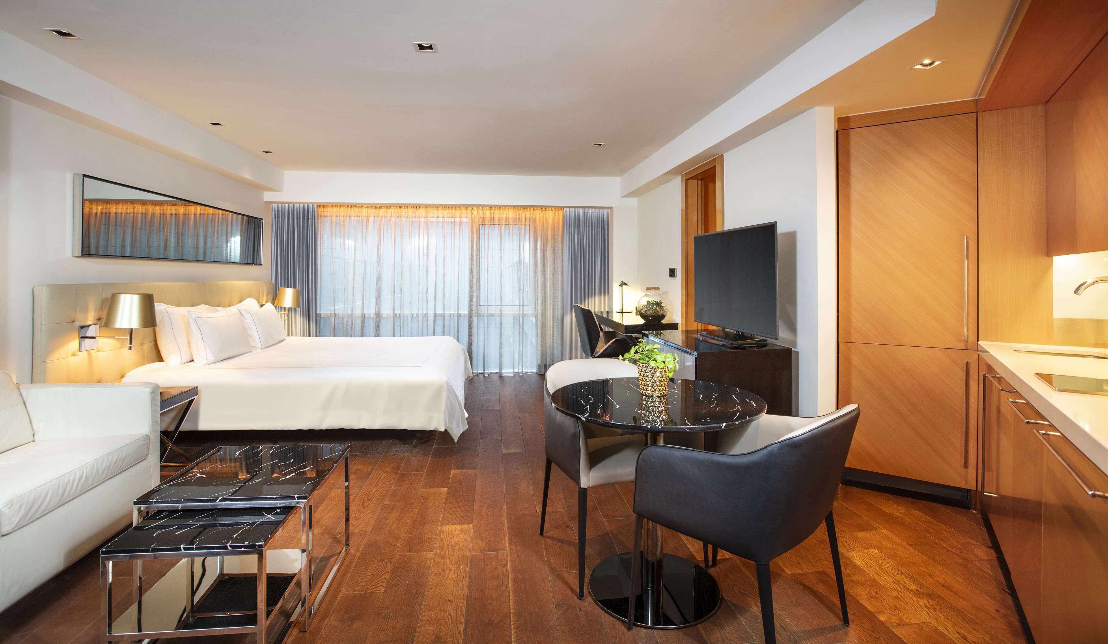 A hotel room with a bed, a desk with a TV, a chair, a sofa, and a dining table.