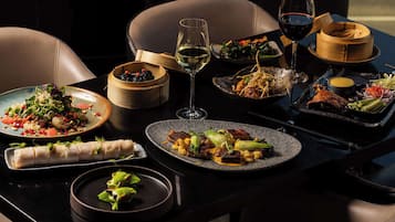 A table set with various dishes, including a rolled appetizer, a salad, and a plate with meat and vegetables, along with two glasses of wine.