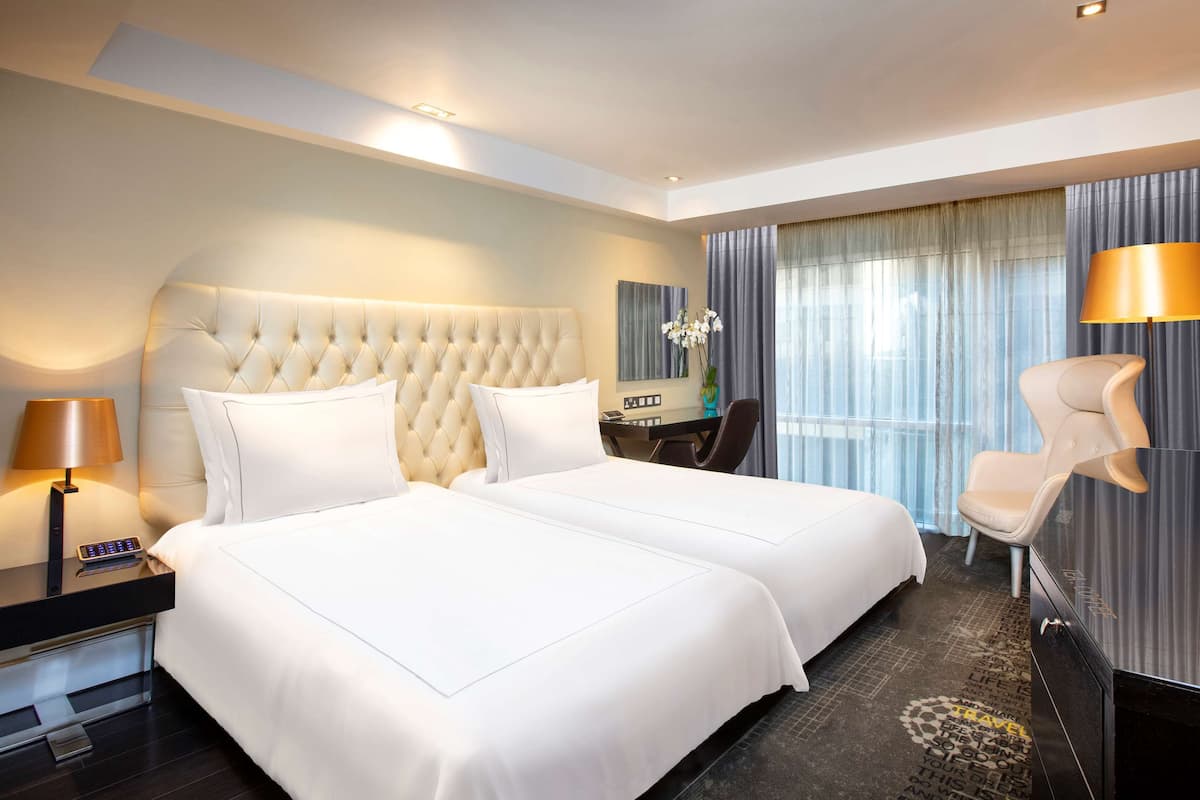 Habitación de hotel con una cama grande, un escritorio con silla, televisor y ventana con cortinas.