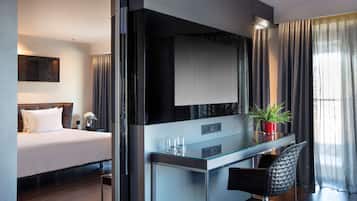 A modern hotel room with a bed, a glass desk, a chair, a TV, and a potted plant.