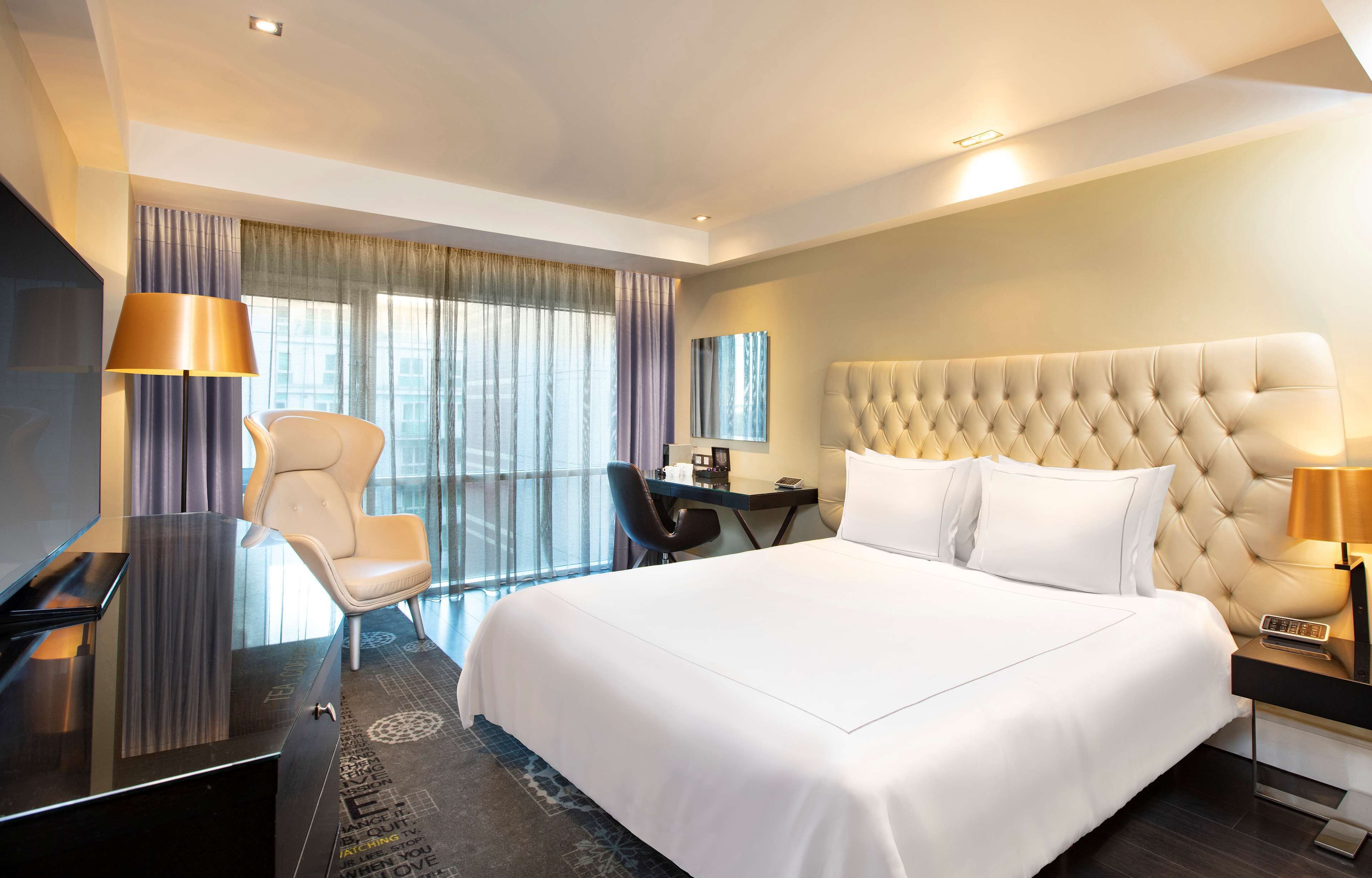 A hotel room with a large bed, a desk, a chair, a TV, and a window with curtains.