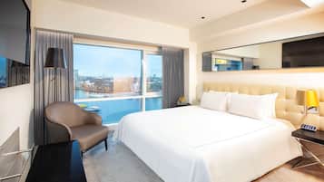 Une chambre d’hôtel avec un grand lit, une chaise, un bureau et une vue sur le paysage urbain, grâce à de grandes fenêtres.