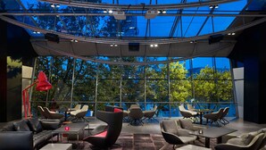 Un espacio interior moderno con techo de vidrio, varias zonas de estar y vistas a árboles.