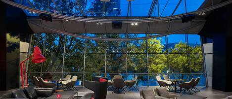 A modern indoor space with a glass ceiling, multiple seating areas, and a view of trees outside.