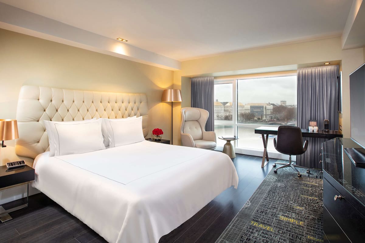 Habitación de hotel con una cama grande, un escritorio, una silla, un televisor y vistas a la ciudad desde la ventana.