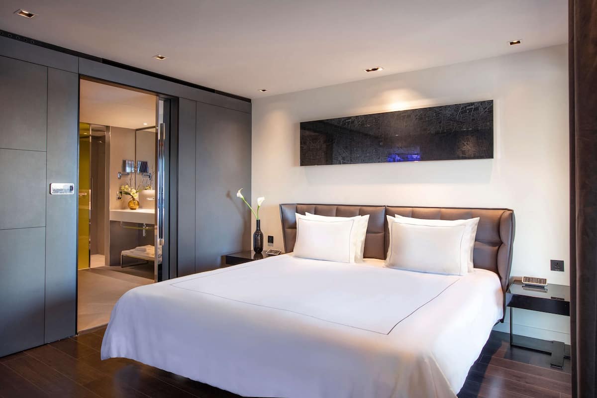 Una habitación de hotel moderna con una cama grande, una mesita de noche y una obra de arte colgada en la pared.