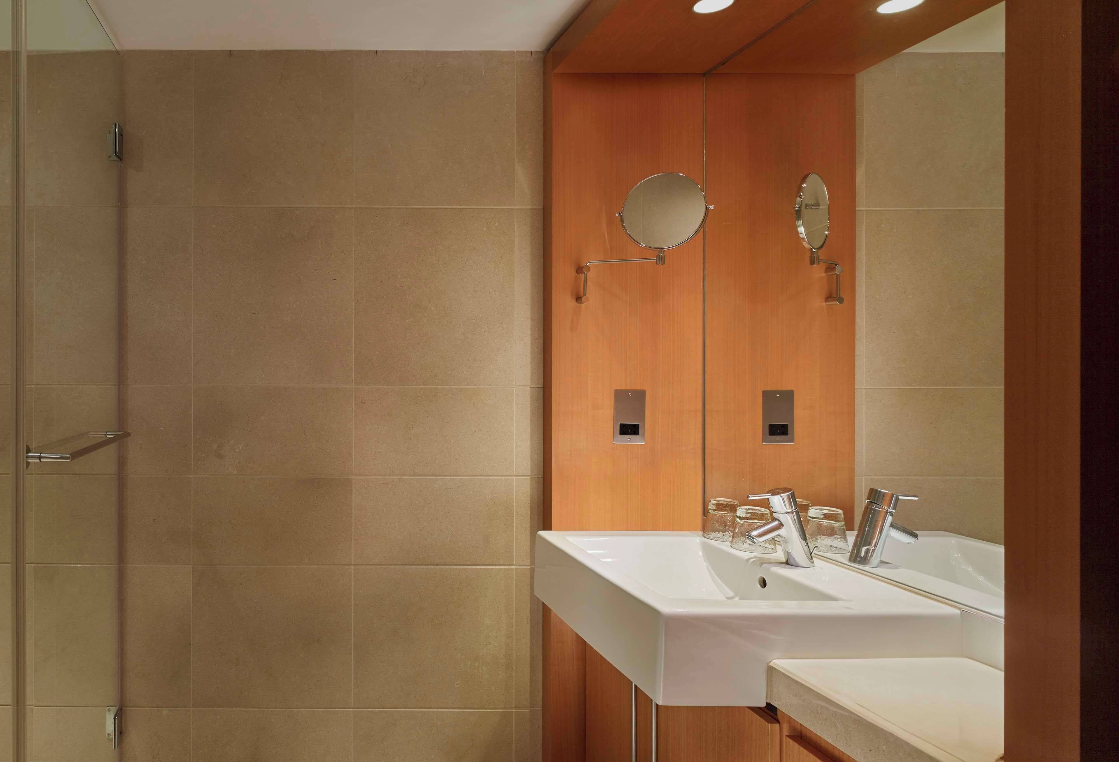A modern bathroom with a large mirror, two sinks, and a shower area.