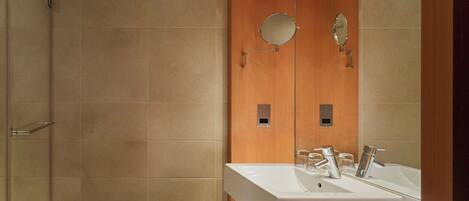 A modern bathroom with a large mirror, two sinks, and a shower area.
