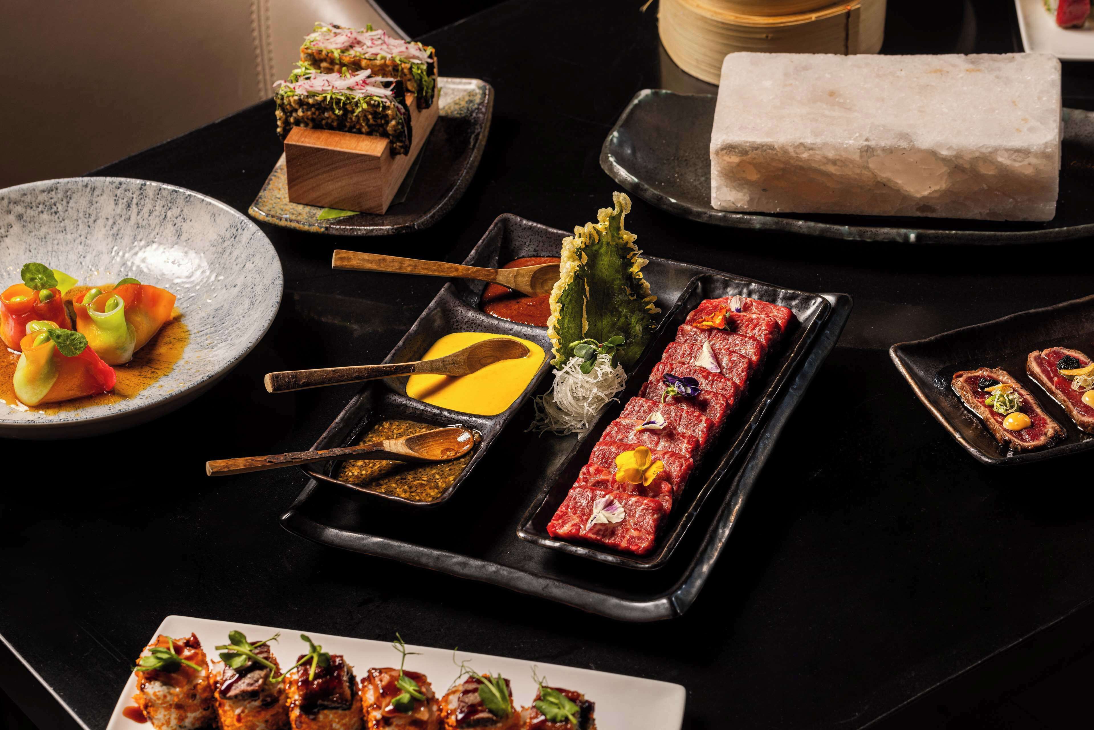 A variety of dishes on a black table, including sushi, sashimi, and a large block of ice.