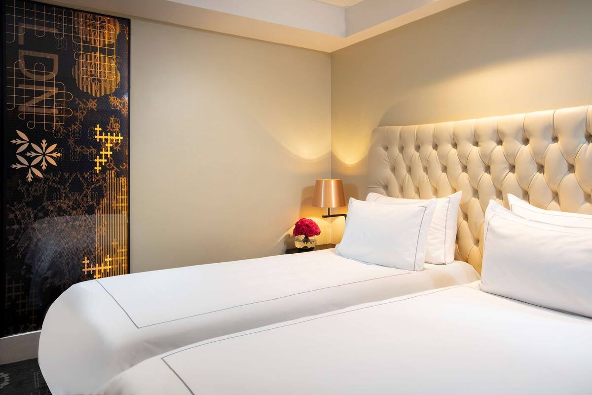 Una habitación de hotel con una cama grande, una mesita de noche con lámpara y un panel decorativo en la pared.