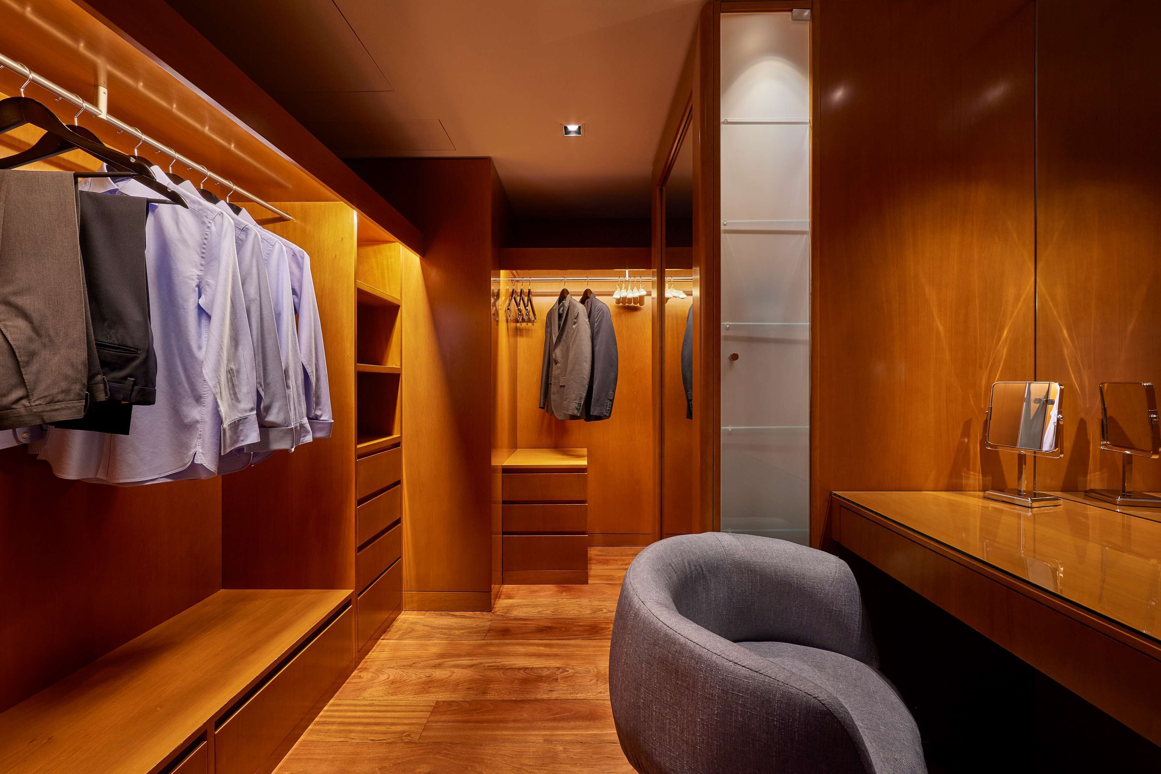 Ein moderner begehbarer Kleiderschrank mit Holzschränken, einer Bank und einem Spiegel.