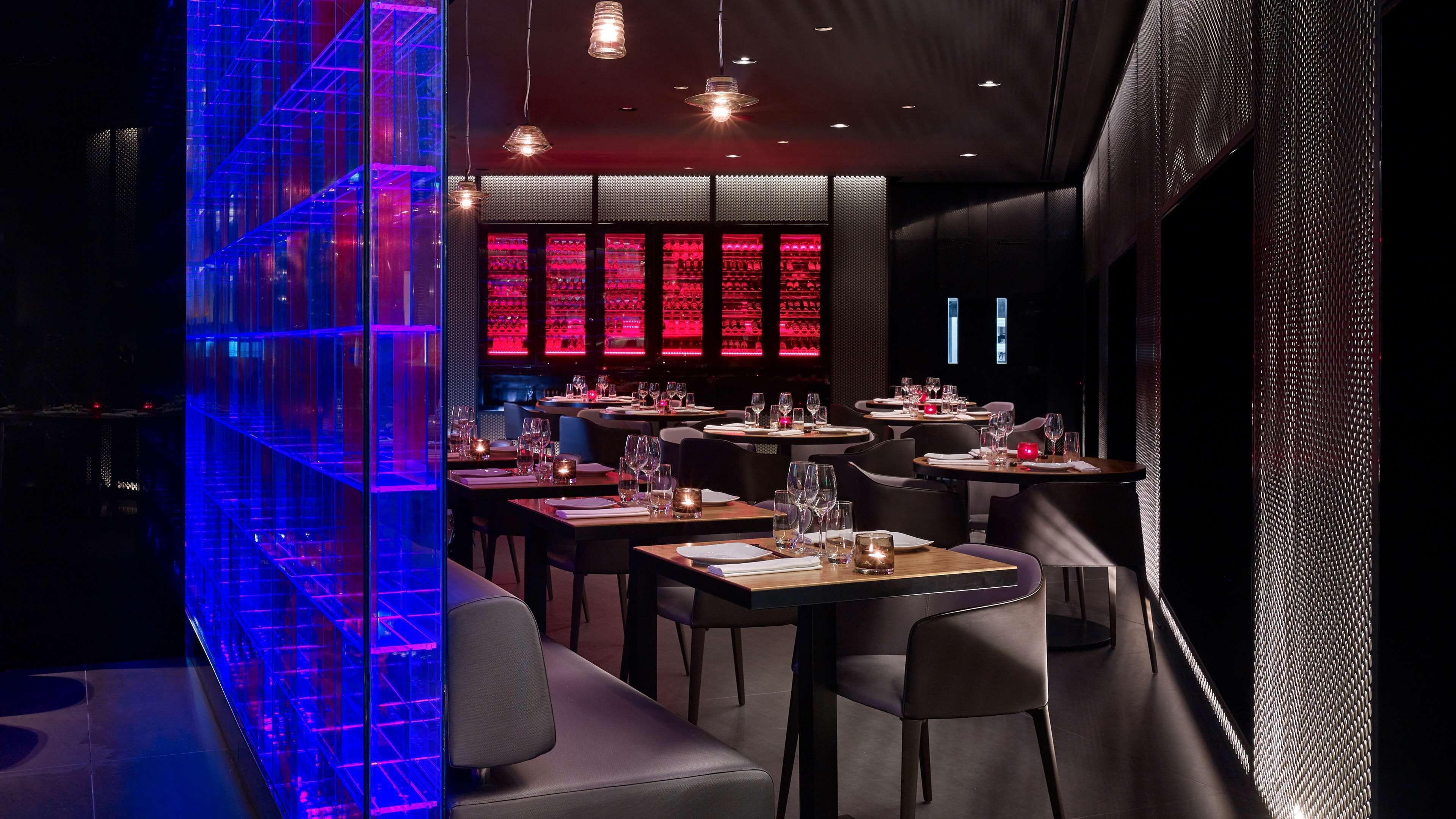 Un interior de restaurante moderno con mesas dispuestas para comer, una zona de bar y una estructura azul iluminada y distintiva.