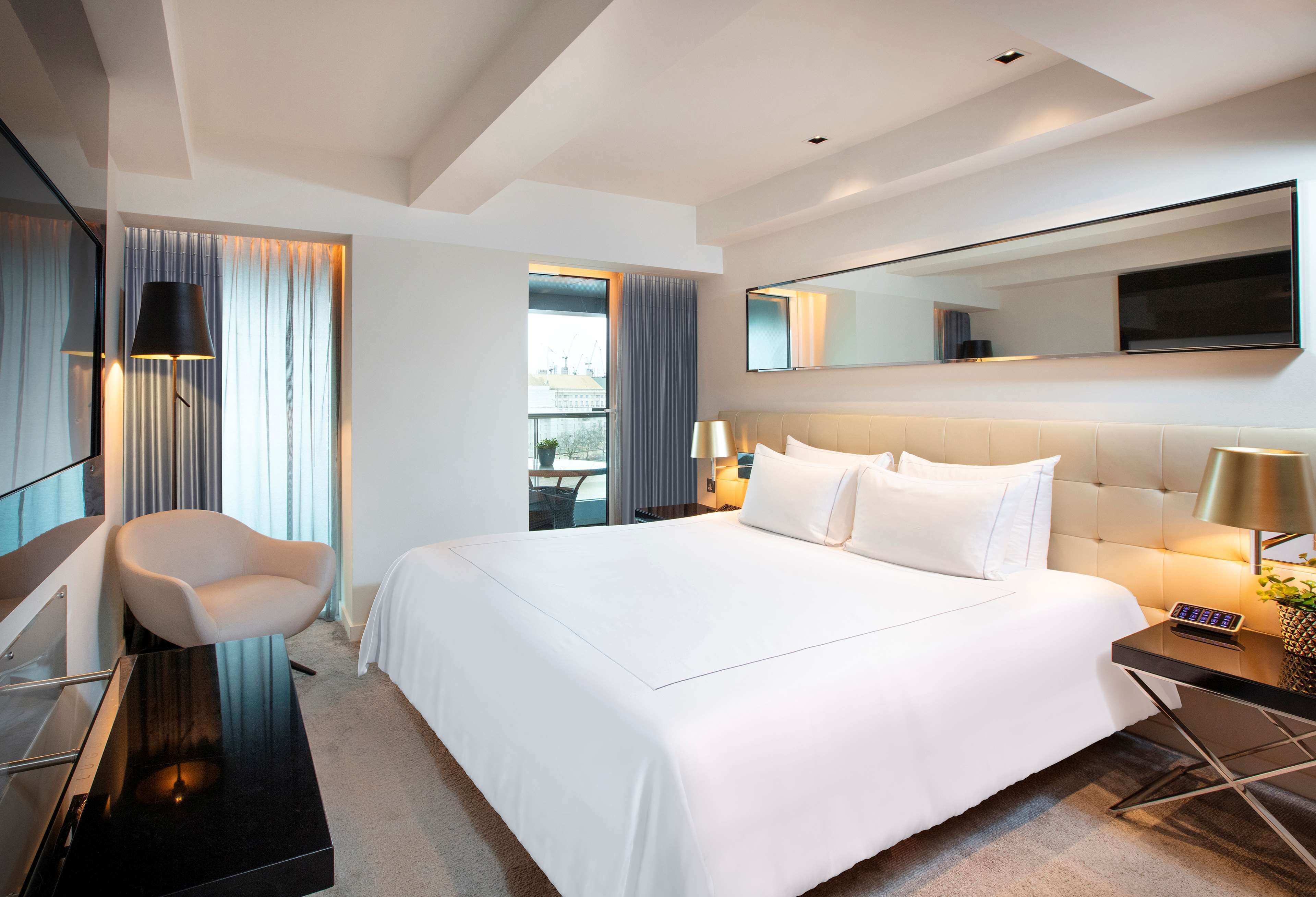 A modern hotel room with a large bed, a chair, a desk, and a large mirror.