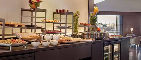 Uma mesa de buffet com diversos alimentos e bebidas, incluindo frutas, doces e sucos.