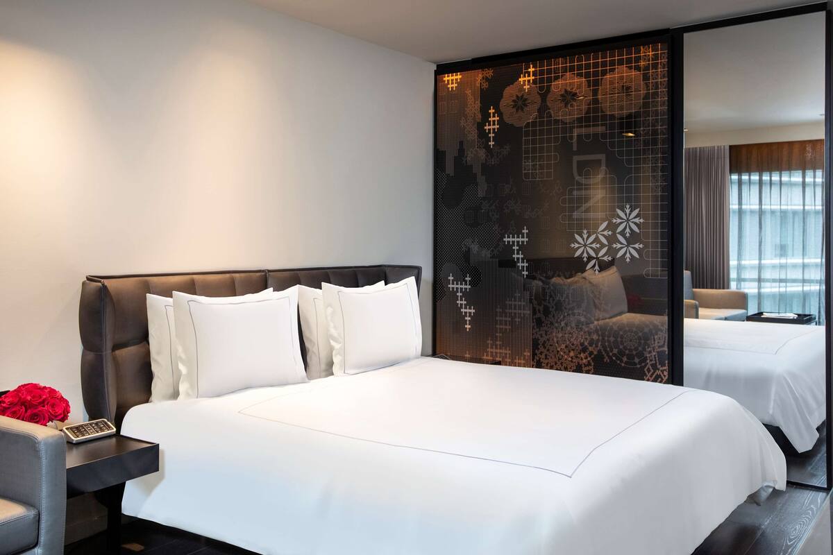 Una habitación de hotel moderna con una cama grande, una mesita de noche y un separador decorativo con un diseño geométrico.