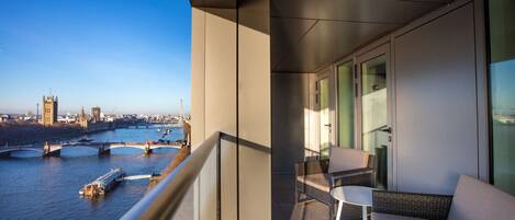 A balcony with wicker furniture, a view of a river, and a cityscape in the background.
