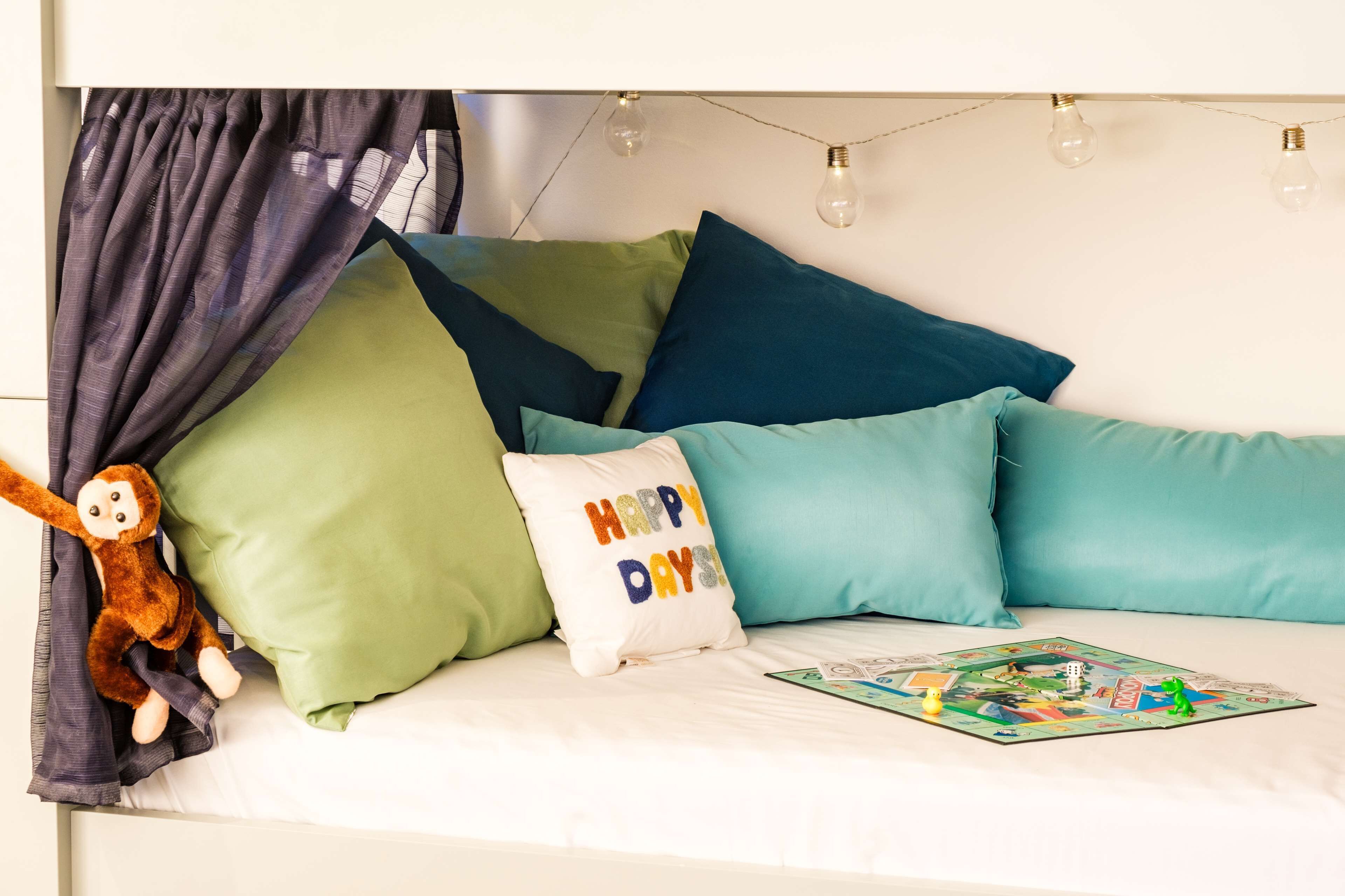 A bed with multiple pillows, a stuffed monkey toy, and a board game.