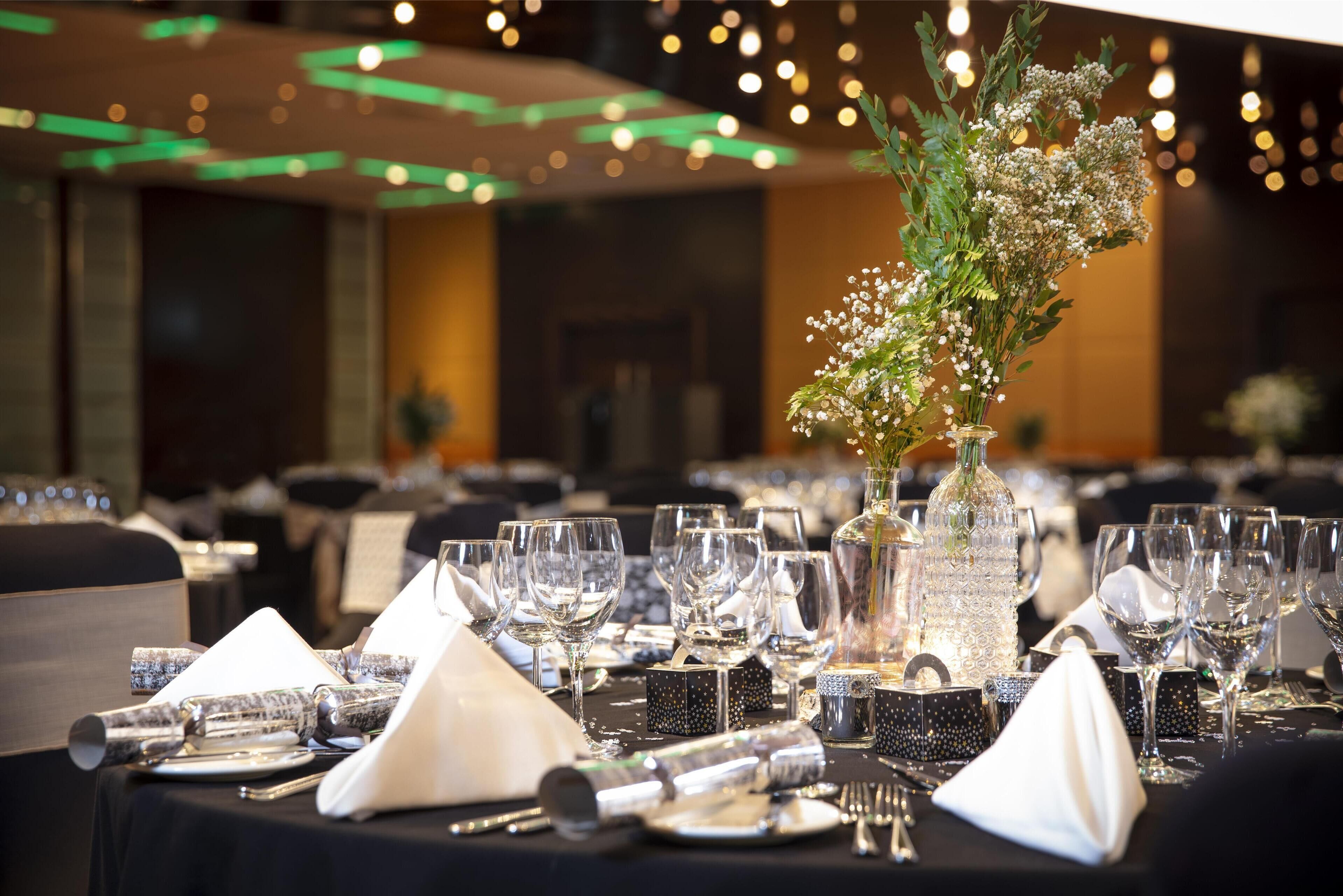 A banquet table set with clear glassware, black napkins, and a decorative floral arrangement in a clear vase.