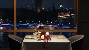 Una mesa dispuesta para dos con vistas a un paisaje urbano, que incluye una torre destacada y un puente.