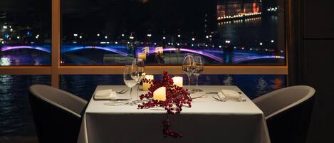 A table set for two with a view of a cityscape, including a prominent tower and a bridge.