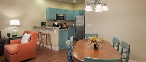 Una cocina moderna con armarios color turquesa, un refrigerador de acero inoxidable y una mesa de comedor de madera con sillas.