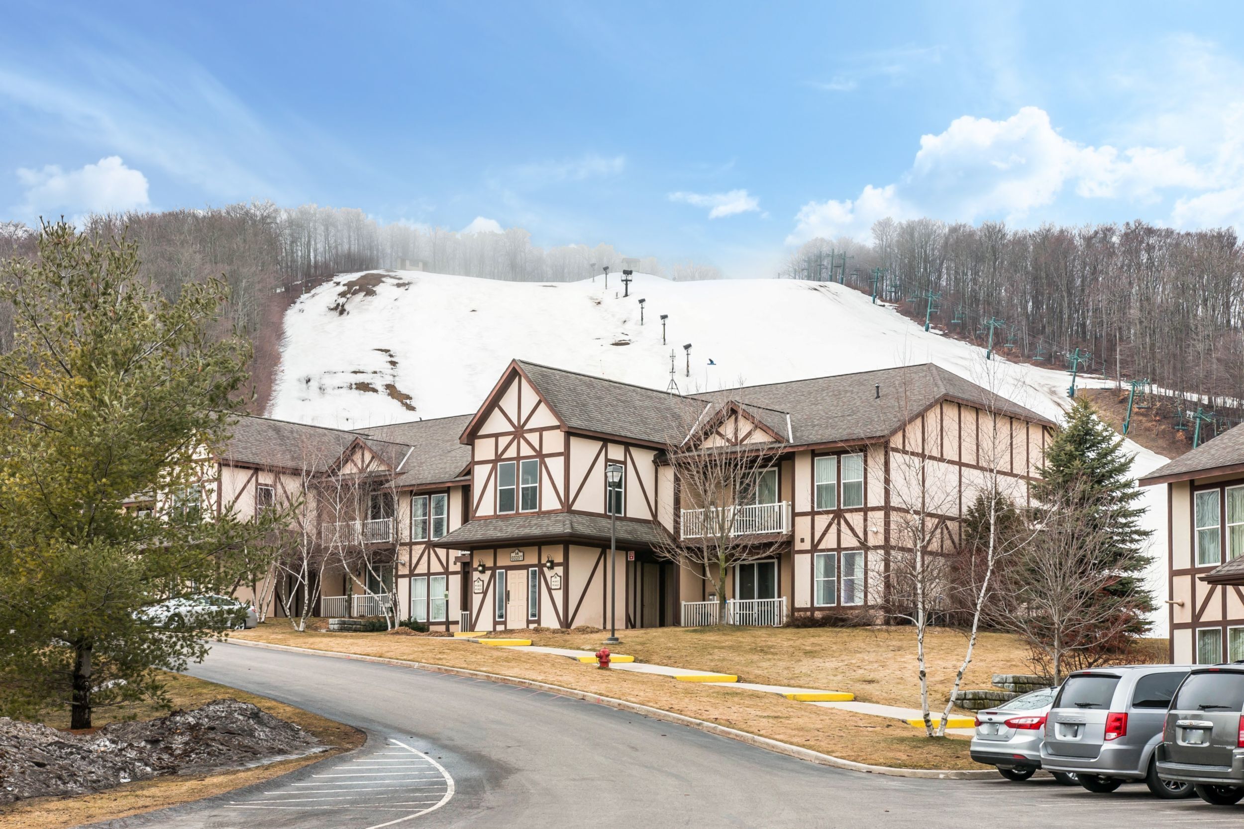 A building with a snow-covered hill in the background, a parking lot with cars, and a clear sky.