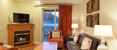 A living room with a fireplace, a television, a sofa, a coffee table, and a view through a sliding door.
