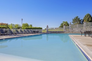 Una piscina rectangular con pared de piedra y valla de metal, rodeada de tumbonas y un pequeño pabellón.