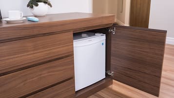 A wooden desk with a built-in refrigerator, a white cup, saucer, and a blue object on the surface.