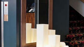 Eine moderne Hotelhalle mit einem Holzbüro, einer roten Vase und einer Sitzecke mit einem blauen Teppich mit Muster.