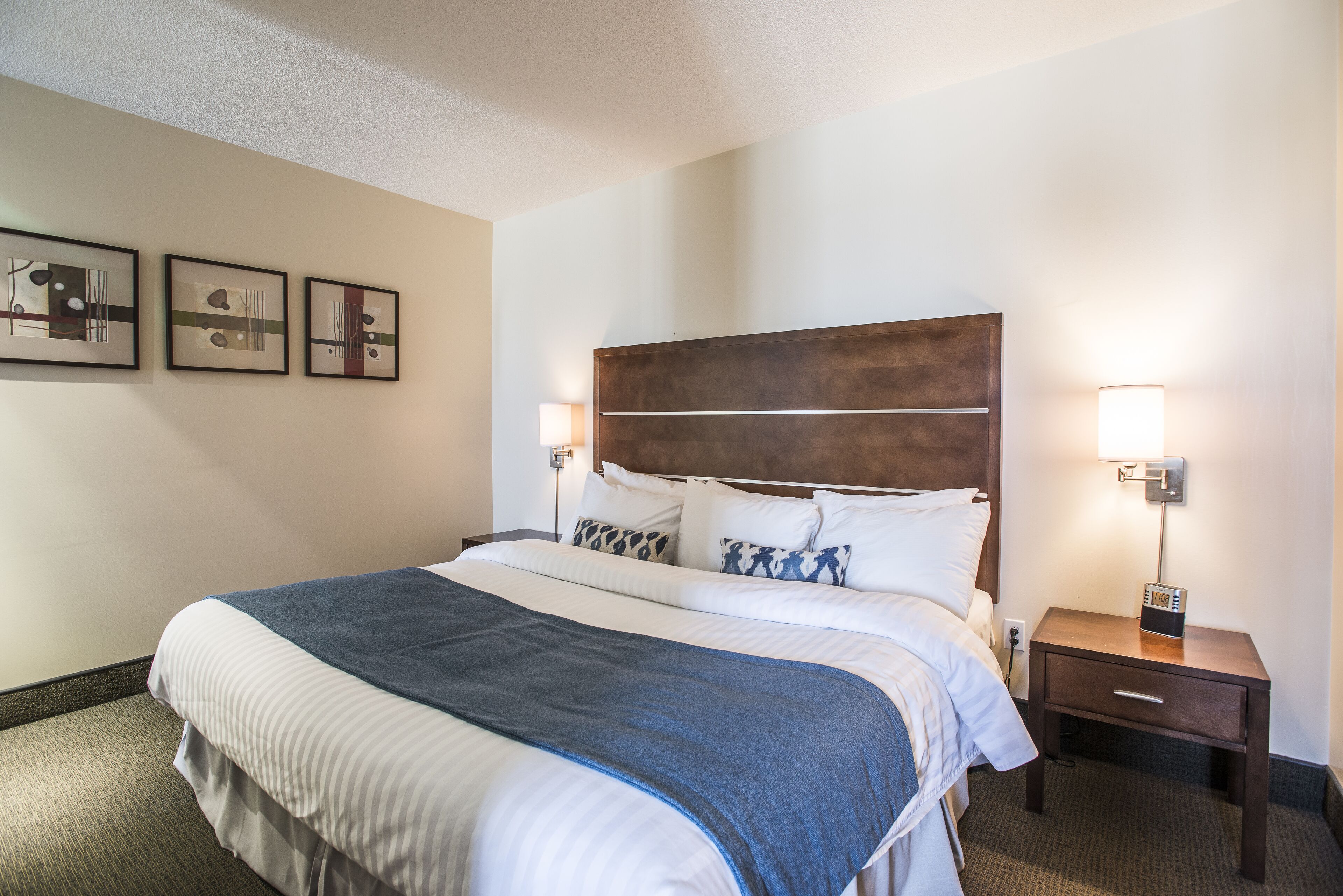 A hotel room with a large bed, two bedside lamps, a nightstand, and three framed pictures on the wall.