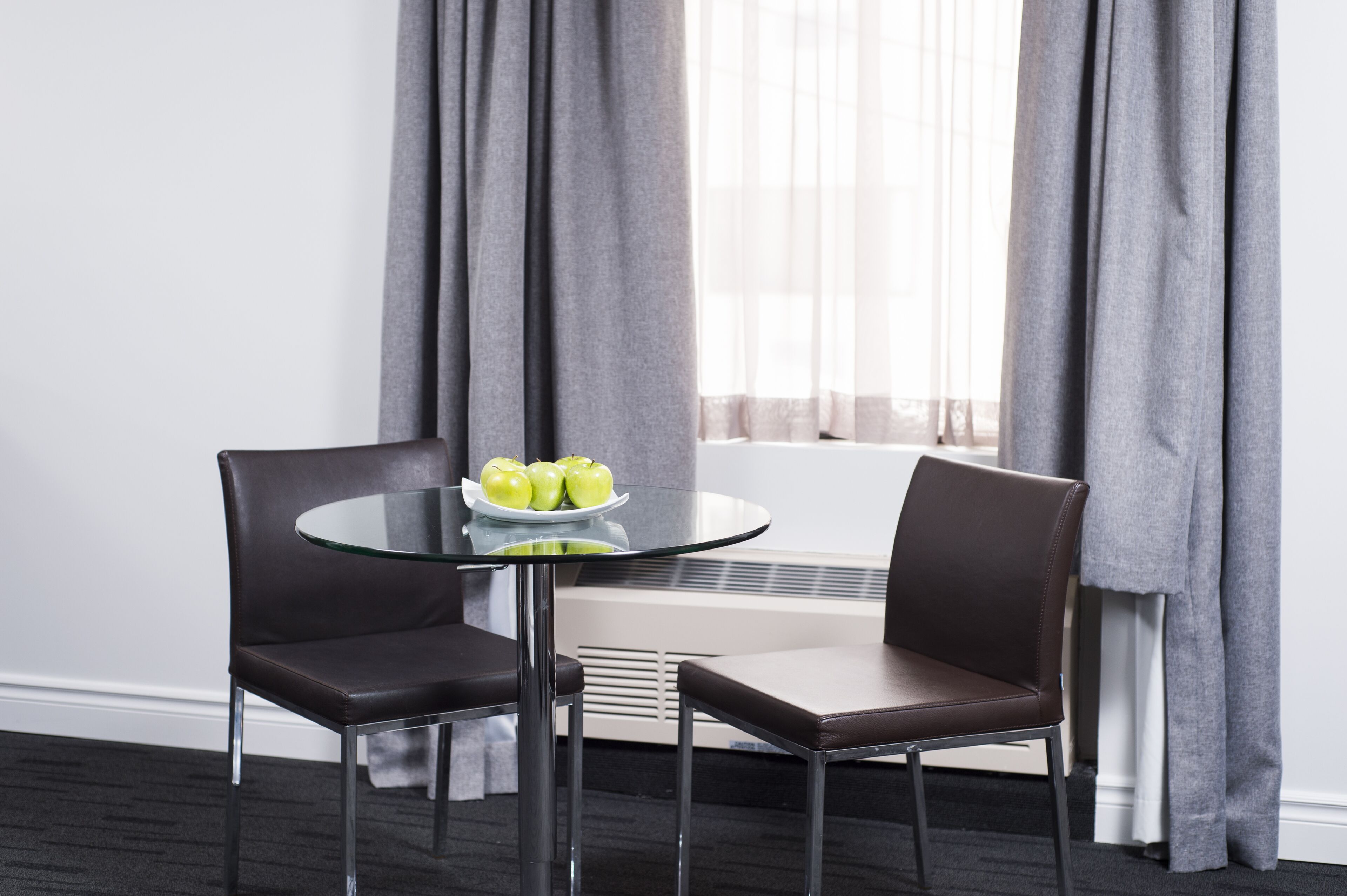Une pièce moderne avec une table en verre, deux fauteuils en cuir et une assiette de pommes vertes.