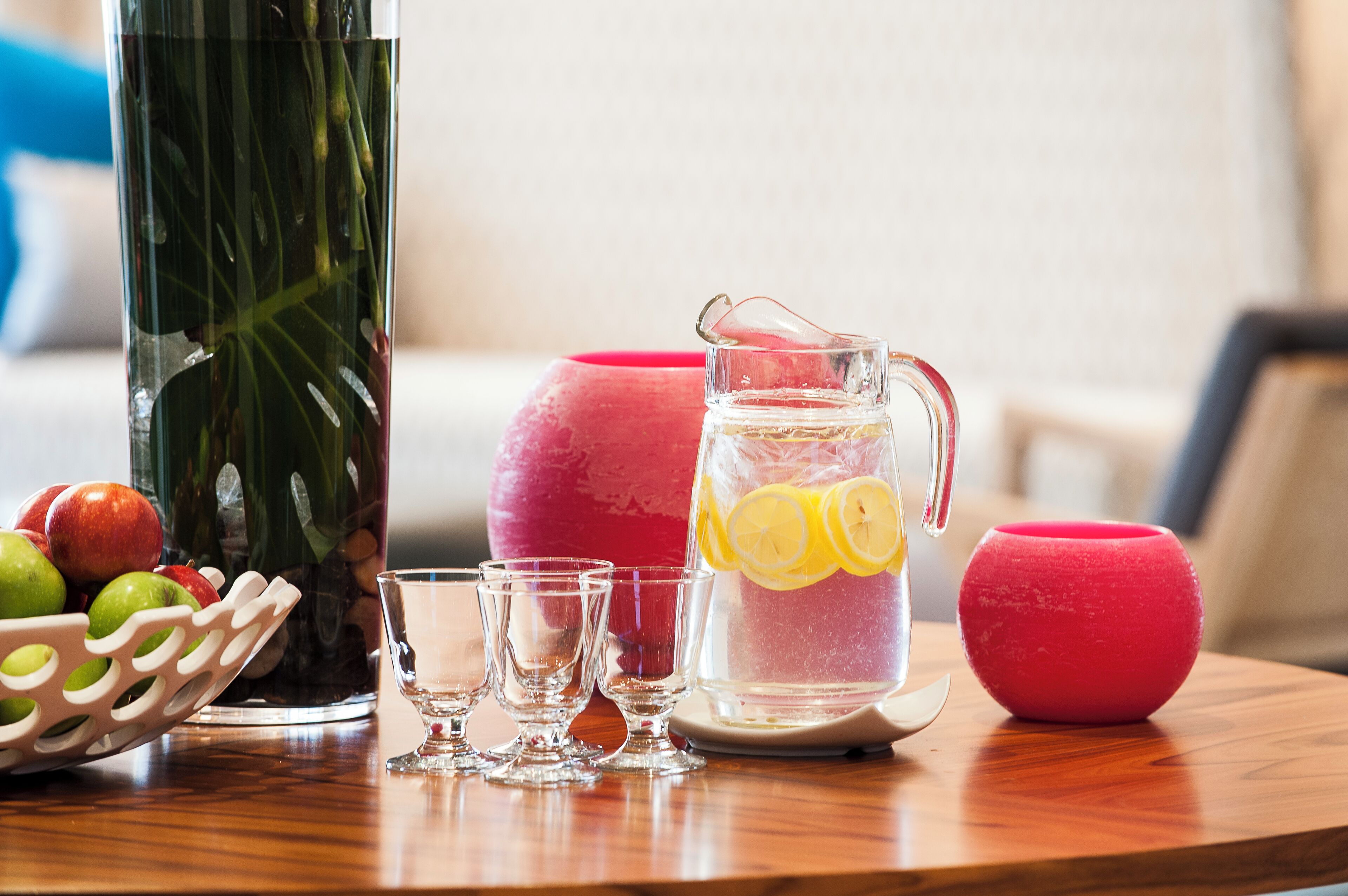 Ein Holztisch mit einer Wasserkaraffe, einem Glas und einer Obstschale, sowie einer roten Kerze.