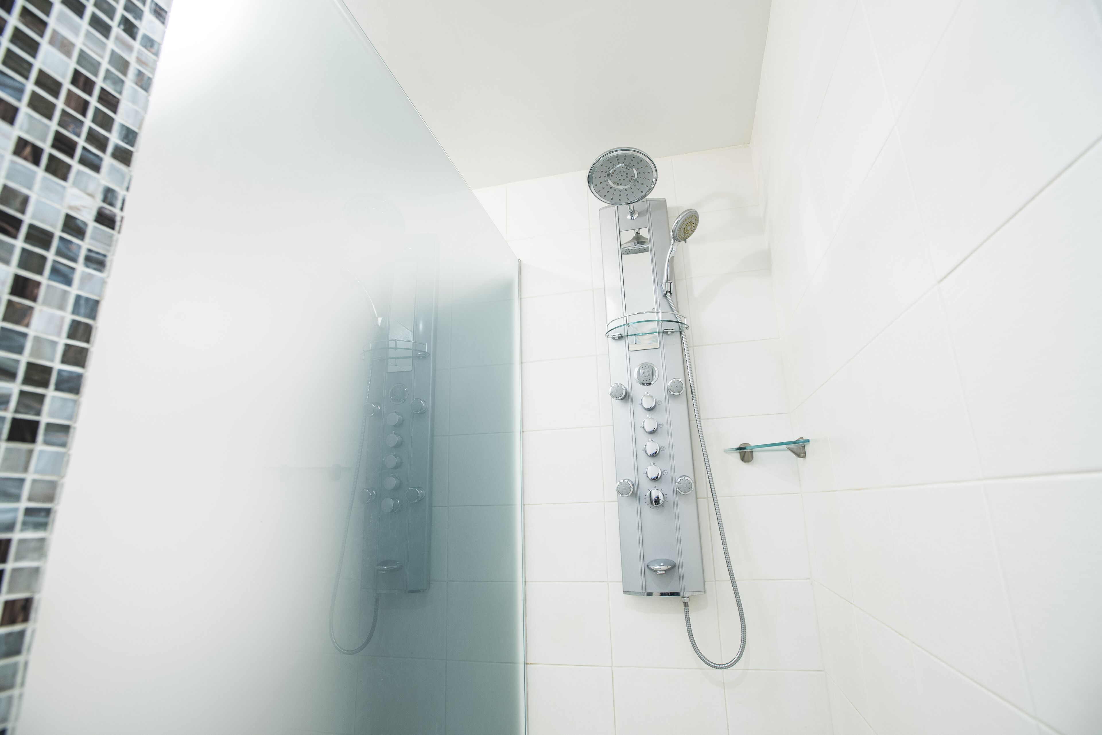 A modern bathroom with a glass-enclosed shower, a handheld showerhead, and a wall-mounted control panel.