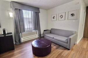 Una sala de estar con un sofá gris, un otoman redondo, una cafetera y una ventana con cortinas.
