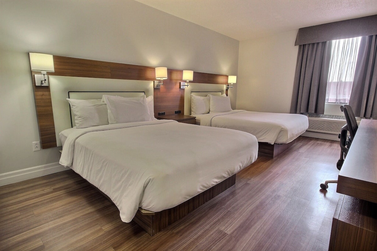 Habitación de hotel con dos camas, un escritorio y una ventana con cortinas.