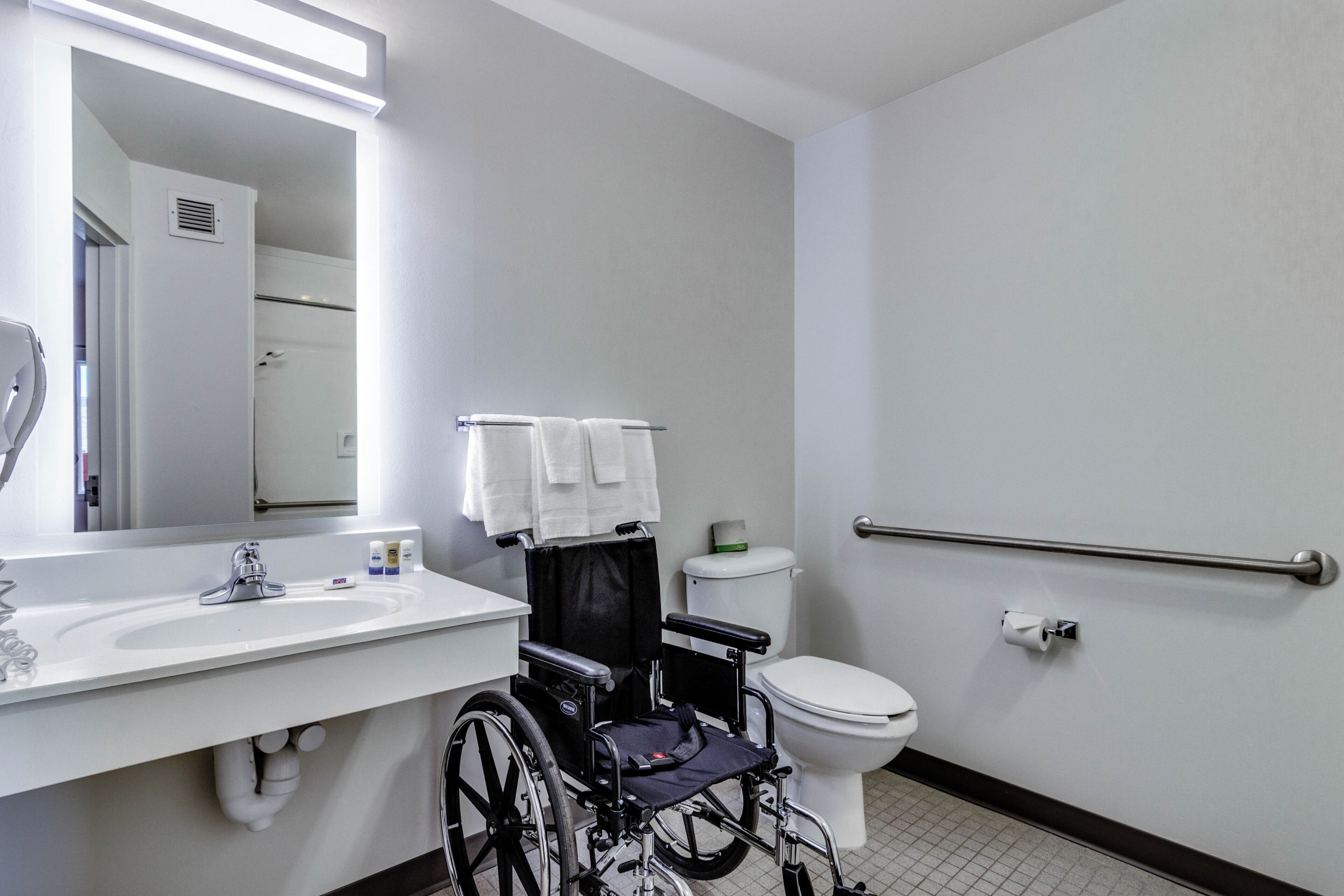 A wheelchair-accessible bathroom with a sink, toilet, and handrail.