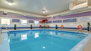Una piscina interior amb aigua cristal·lina, una cadira de socorrista i un cartell amb les normes de la piscina.