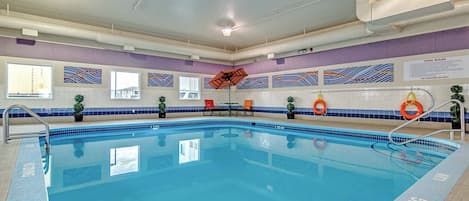 Una piscina interior con agua cristalina, una silla de salvavidas y un cartel con las normas de la piscina.