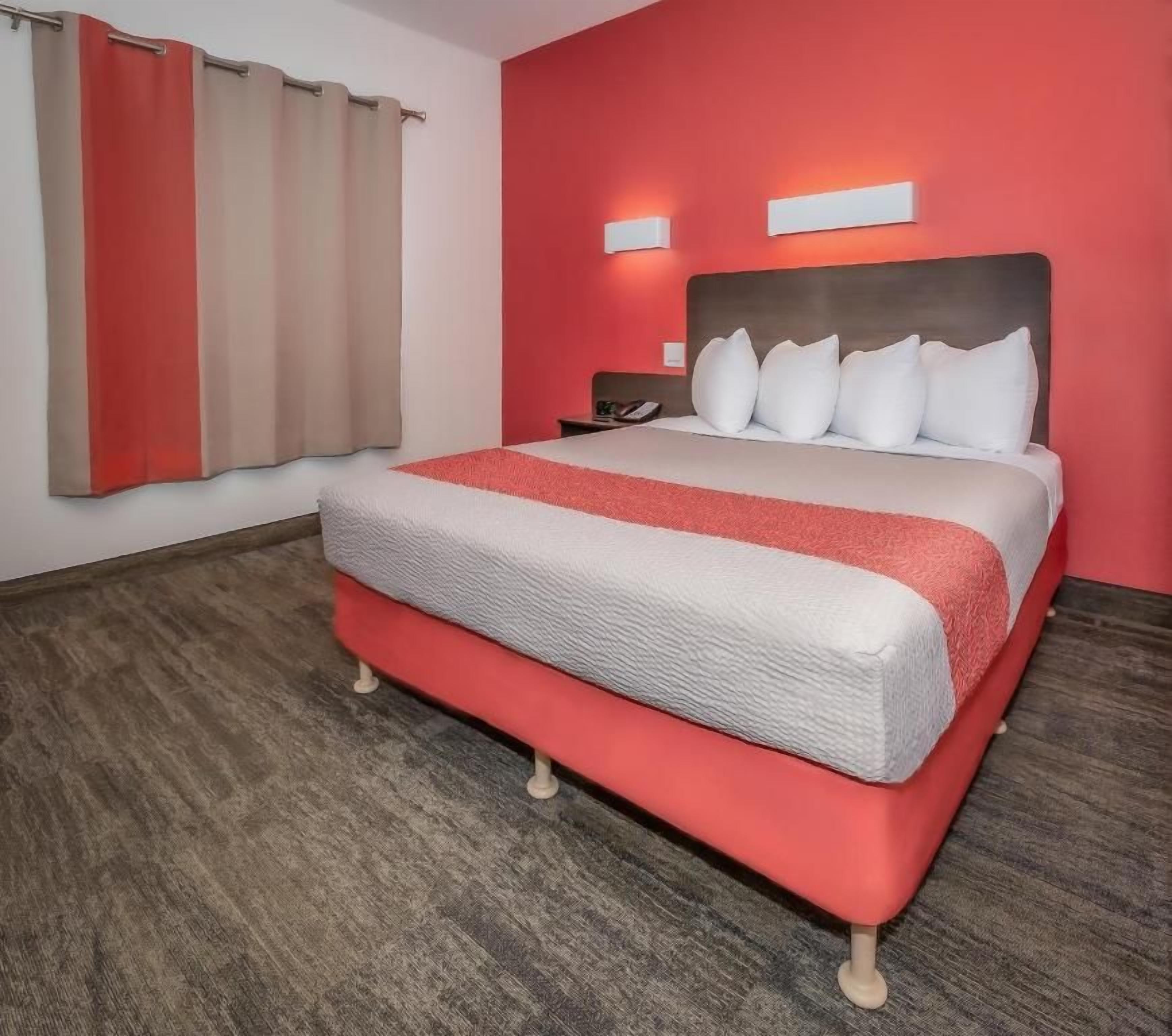 Una habitación de hotel con una cama, una mesita de noche, un teléfono y una ventana con cortinas.