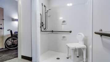 A wheelchair-accessible shower room with a white chair, grab bars, and a handrail.