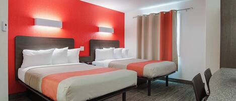 A hotel room with two beds, a small table, and a window with curtains.