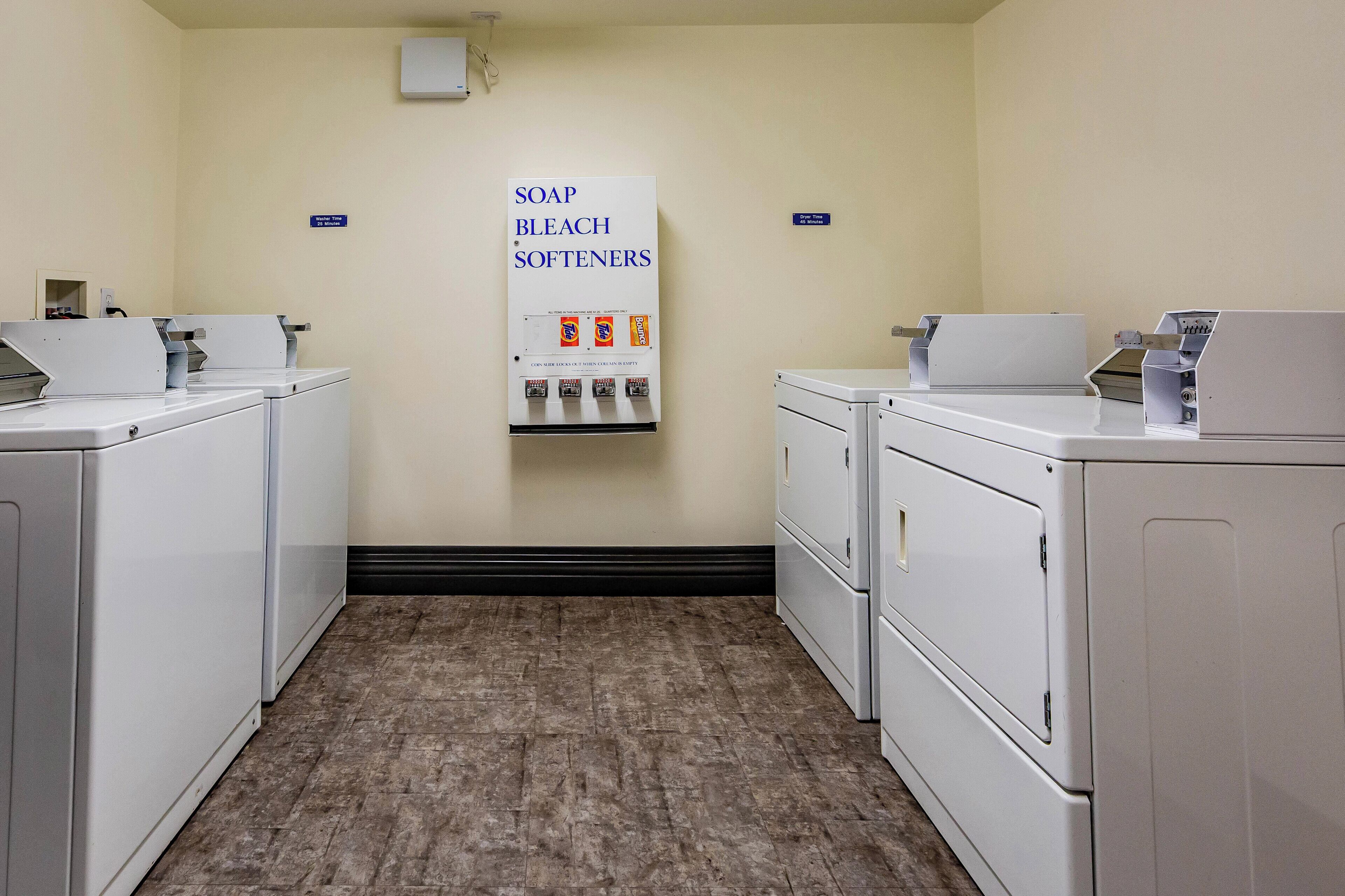 A laundry facility with washers and dryers, a soap and bleach softener dispenser, and a sign indicating the location.