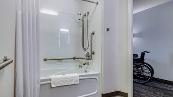 A wheelchair-accessible shower with a grab bar, a white bathtub, and a wheelchair in the adjacent room.